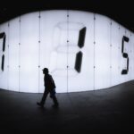photo of man walking near LED signage with numbers