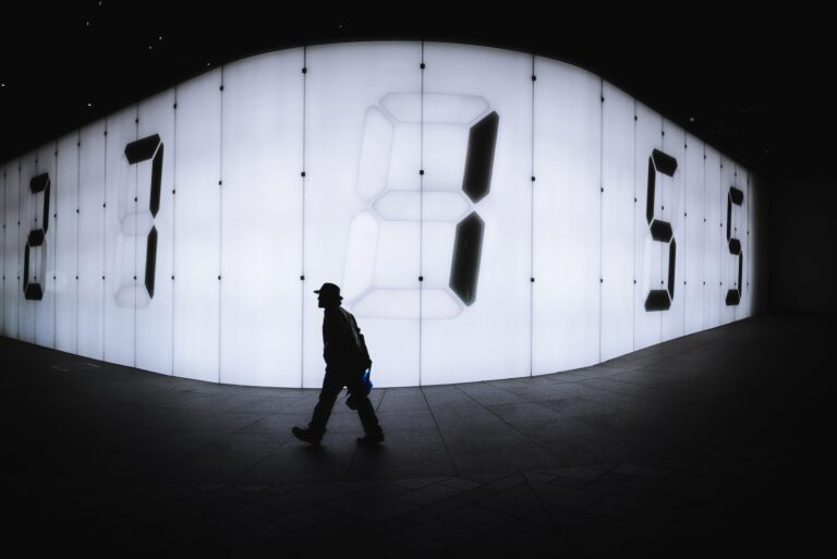 photo of man walking near LED signage with numbers
